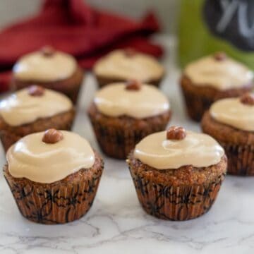 Cupcakes topped with hazelnut frosting and a whole hazelnut sit enticingly on a marble surface, reminiscent of delectable hazelnut flour muffins.