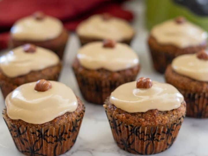 Cupcakes topped with hazelnut frosting and a whole hazelnut sit enticingly on a marble surface, reminiscent of delectable hazelnut flour muffins.