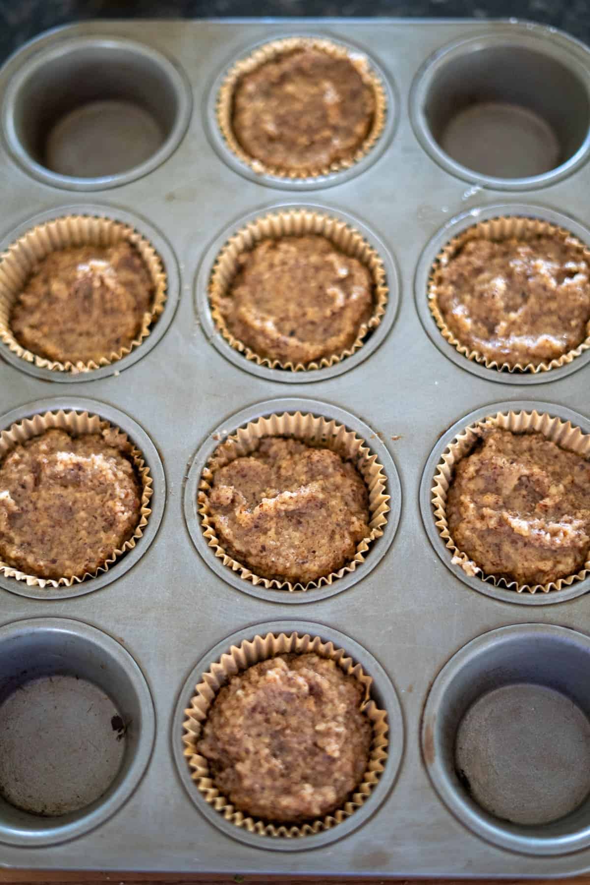 A muffin tray filled with nine unbaked hazelnut muffins nestled in paper liners.