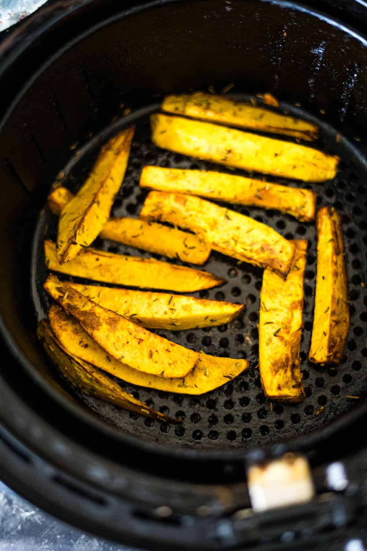 Air fryer basket containing golden-brown, seasoned potato wedges and butternut squash fries.