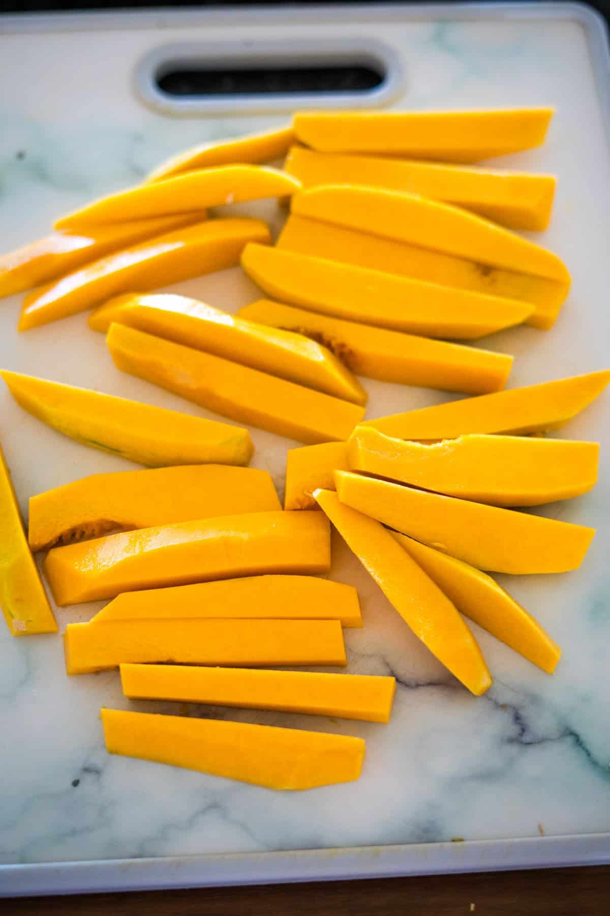 Sliced pieces of yellow squash arranged on a white cutting board with a marble-like pattern, resembling butternut squash fries.