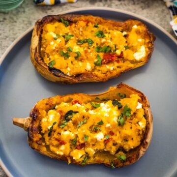 Two halves of a baked stuffed butternut squash filled with a mixture of mashed squash, herbs, and cheese are served on a gray plate.