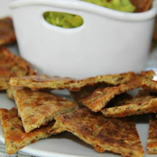 A plate of nacho chips with broccoli and guacamole.