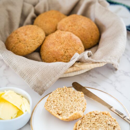 A basket of flaxseed rolls and butter on a white plate.