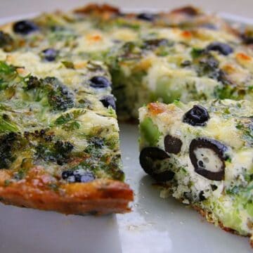 A close-up of a vegetable quiche with a slice missing, revealing ingredients similar to those in a broccoli frittata—broccoli, black olives, and cheese.