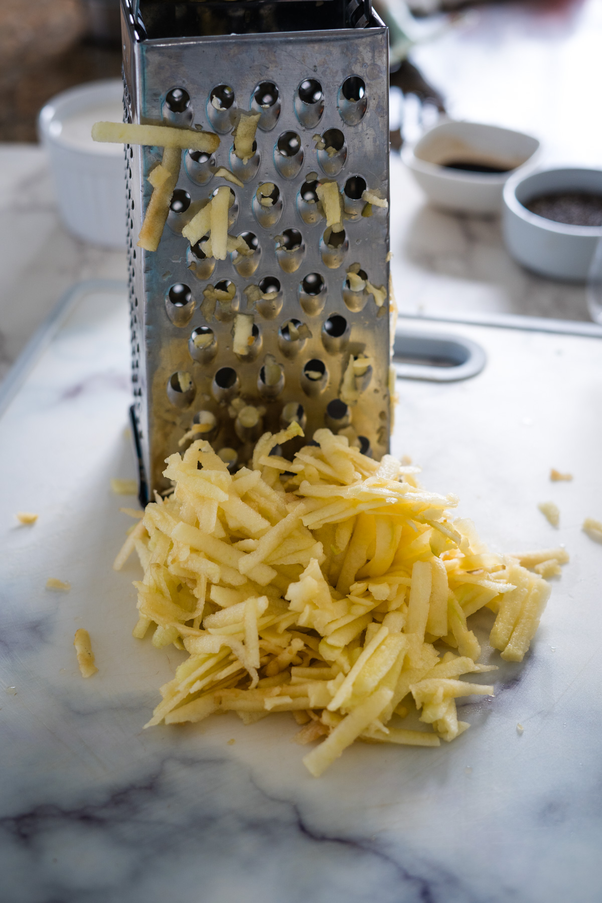 A grater full of shredded potatoes on a cutting board with grated chia sprinkled on top.
