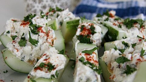 Cucumber bites topped with feta cheese and herbs on a plate.