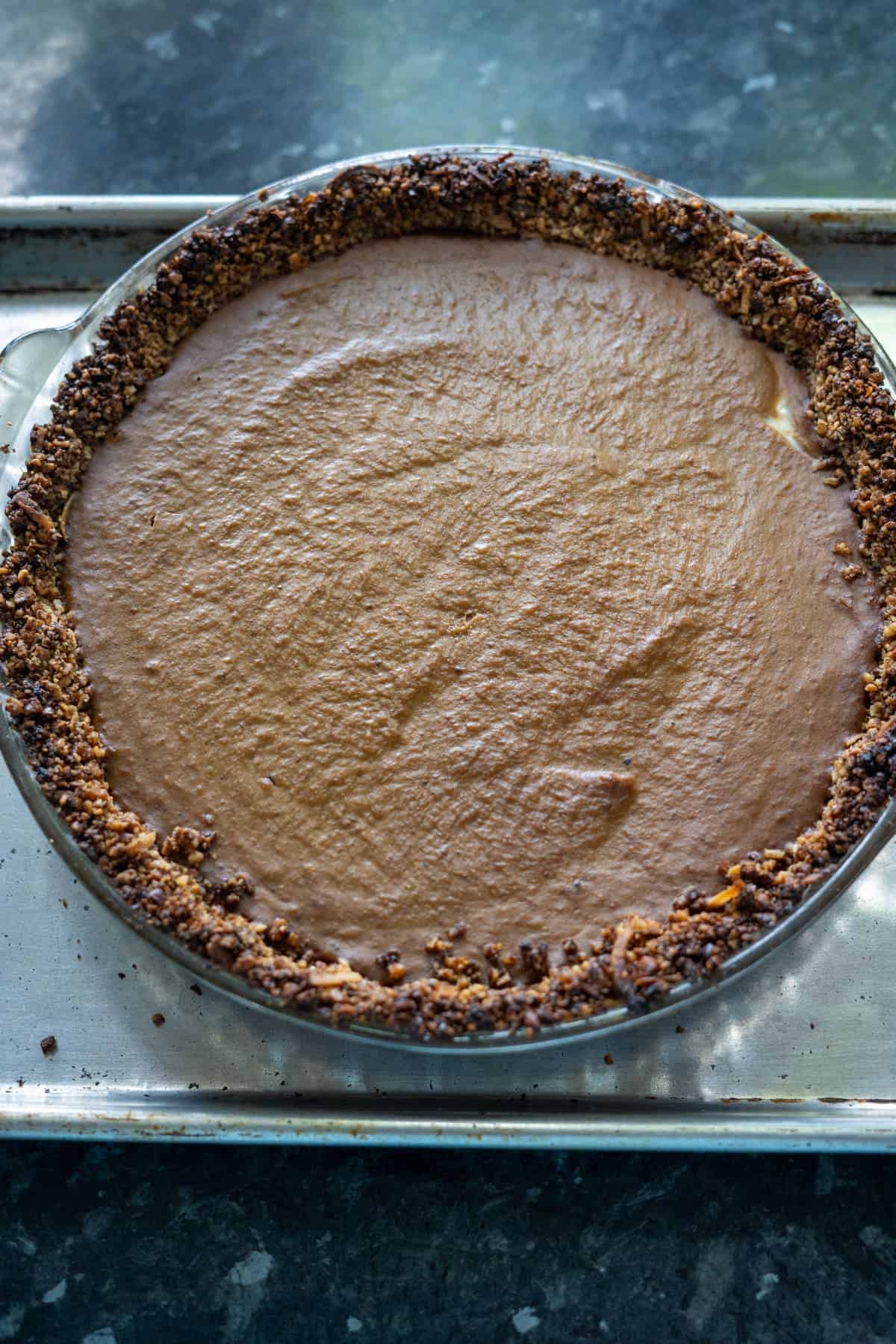 A chocolate pie with a crumbly walnut crust sits on a metal baking tray.