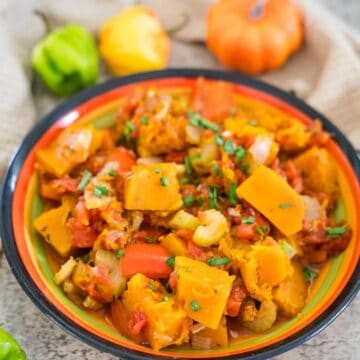 A colorful bowl of seasoned, cooked vegetables featuring Caribbean pumpkin, squash, carrots, bell peppers, and onions, garnished with chopped herbs.