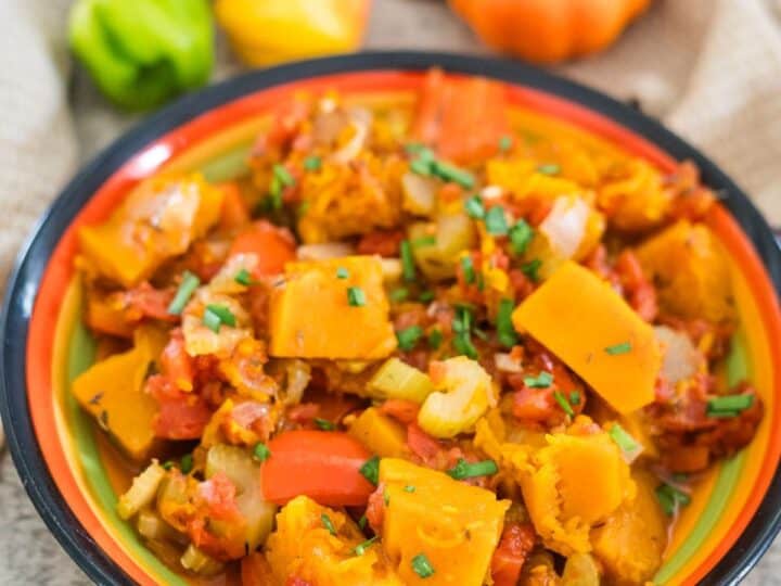 A colorful bowl of seasoned, cooked vegetables featuring Caribbean pumpkin, squash, carrots, bell peppers, and onions, garnished with chopped herbs.