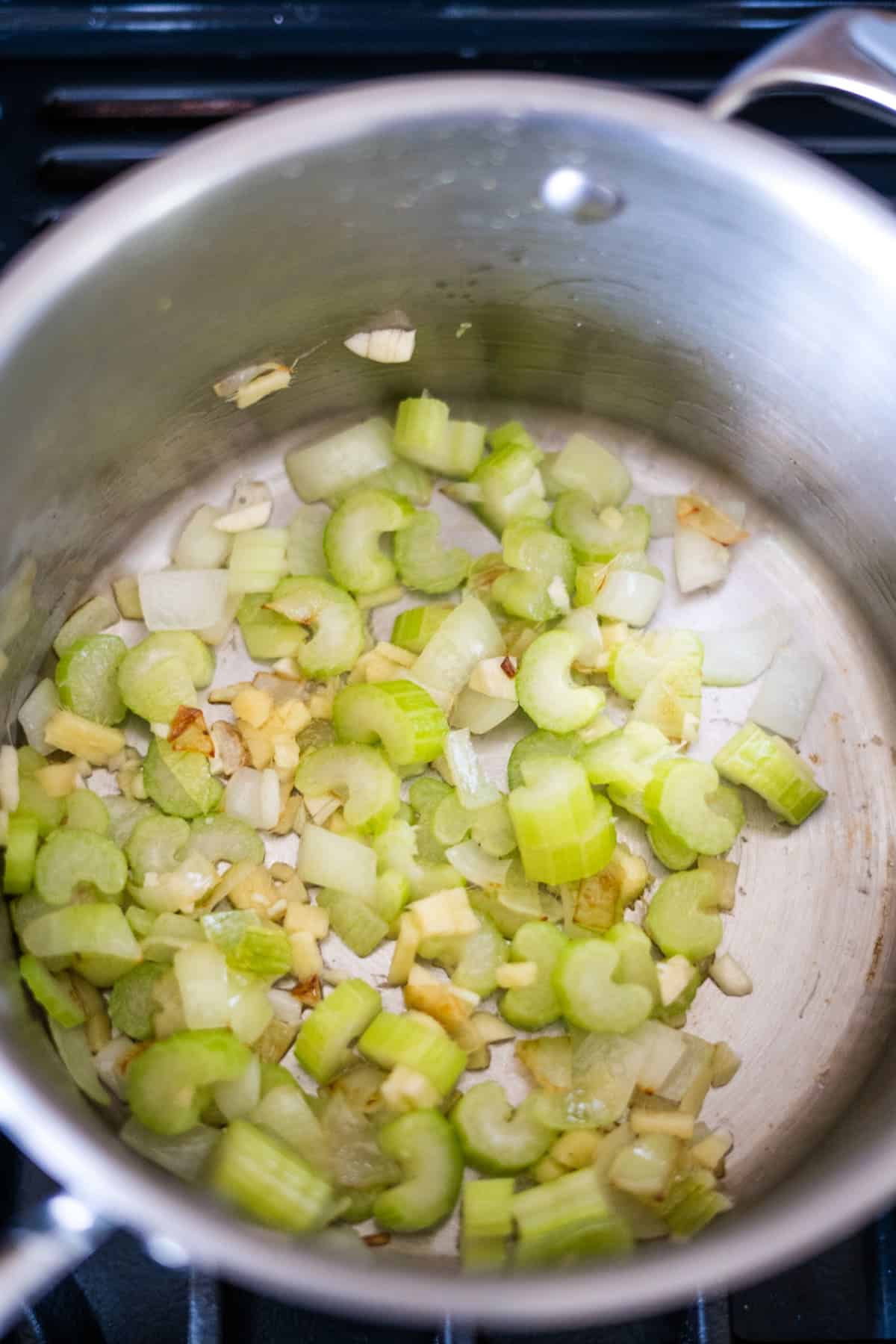 A stainless steel pot with chopped celery, onions, and garlic being sautéed on a stovetop, releasing a mouthwatering aroma. Adding a touch of Caribbean spiced pumpkin elevates the dish with an exotic twist.