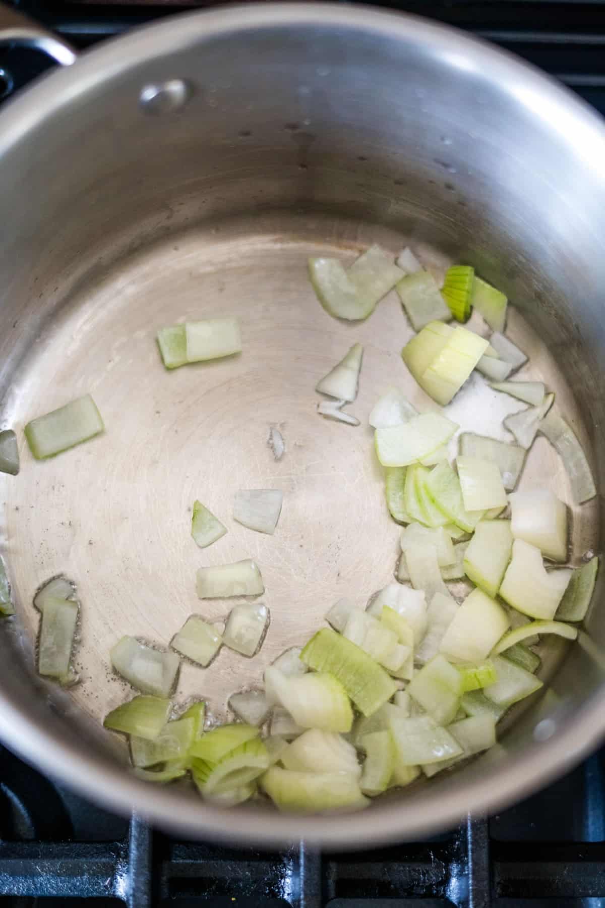 A stainless steel pot with diced onions and Caribbean Spiced Pumpkin starting to sauté inside on a stovetop.