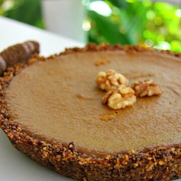 A round walnut pumpkin pie with a nutty crust, topped with whole walnuts, is displayed on a white plate.