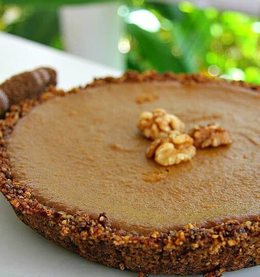 A round walnut pumpkin pie with a nutty crust, topped with whole walnuts, is displayed on a white plate.