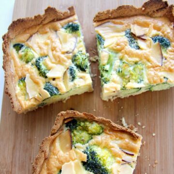 Homemade broccoli quiche with slices of red onion, served on a wooden cutting board.