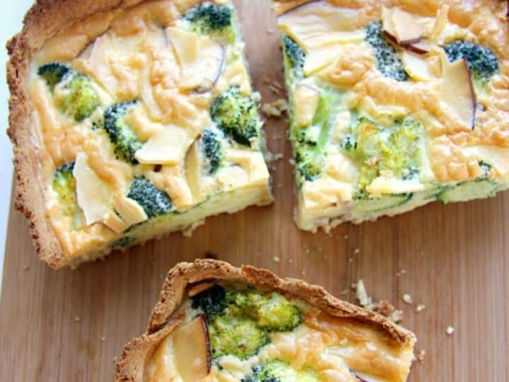 Homemade broccoli quiche with slices of red onion, served on a wooden cutting board.