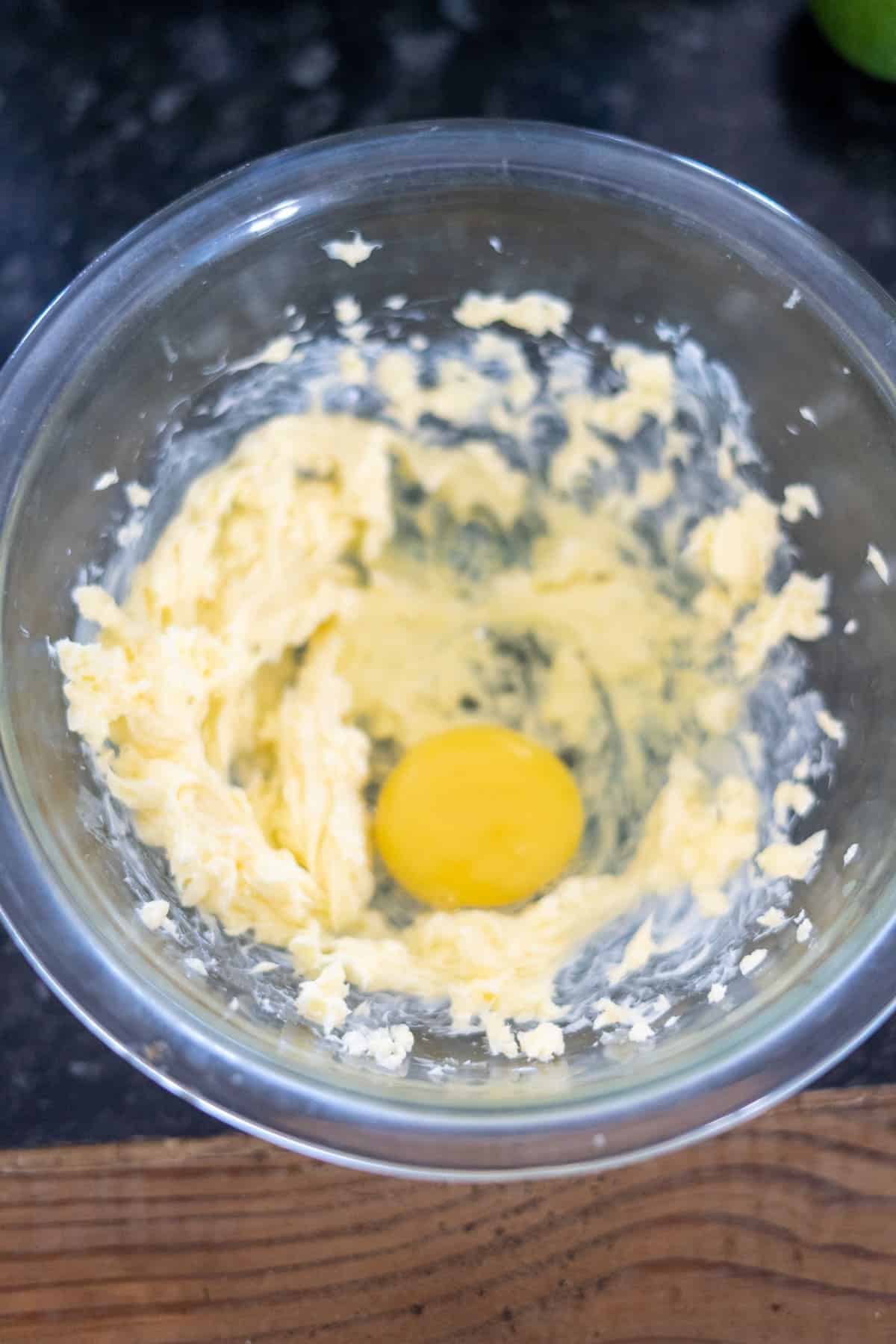 A glass bowl with softened butter and a raw egg awaits on the dark countertop, ready to be transformed into a delicious ginger cake.