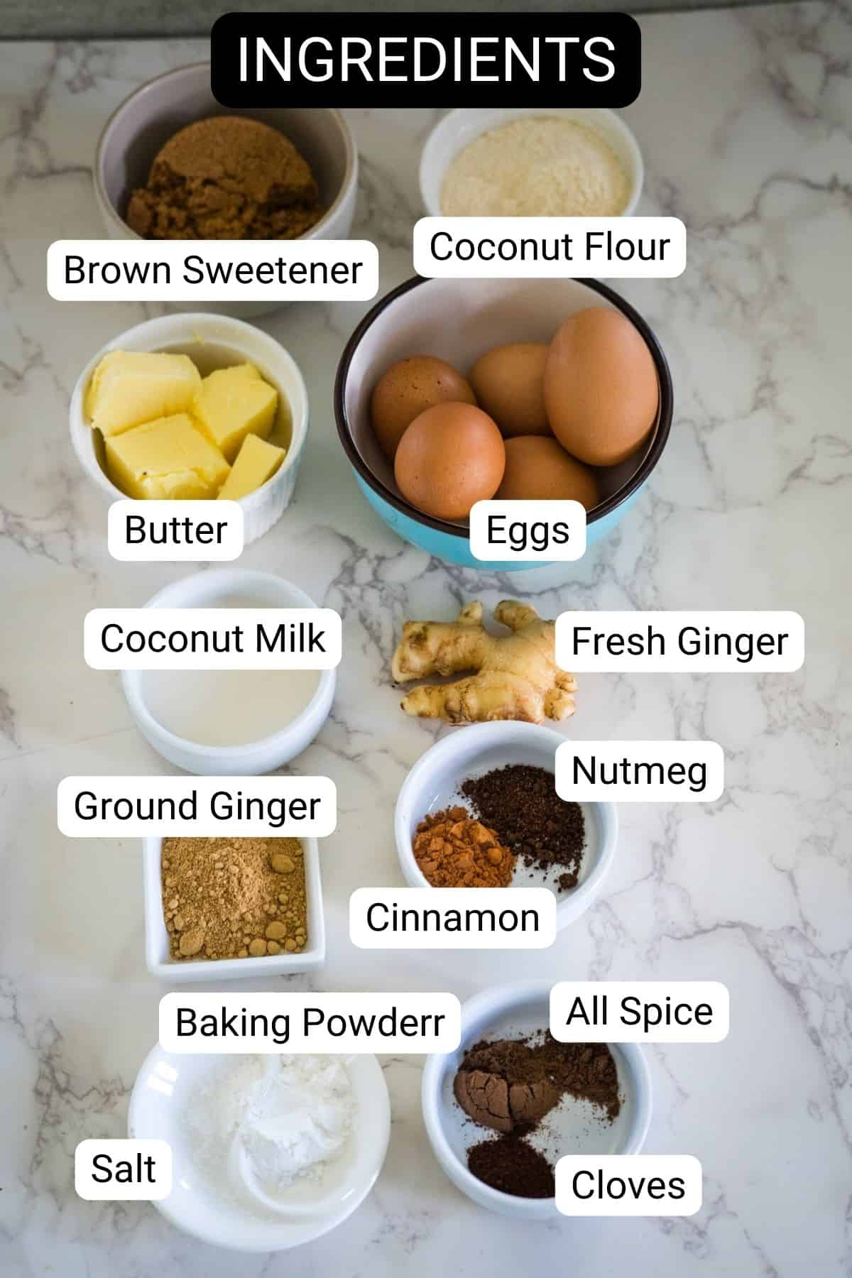 Ingredients for a delightful ginger cake are neatly arranged on a marble surface: brown sweetener, coconut flour, butter, eggs, coconut milk, fresh and ground ginger, nutmeg, cinnamon, allspice, cloves, baking powder, and salt.