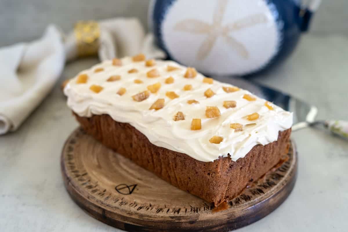 Ginger cake loaf with cream cheese frosting, adorned with candied ginger pieces, elegantly placed on a wooden board.