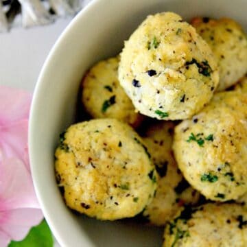 A white bowl with a bowl of cauliflower meatballs and flowers.