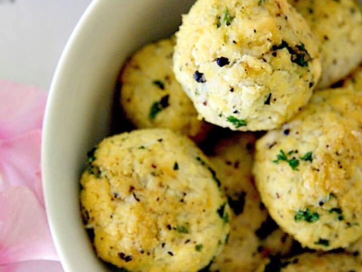 A white bowl with a bowl of cauliflower meatballs and flowers.