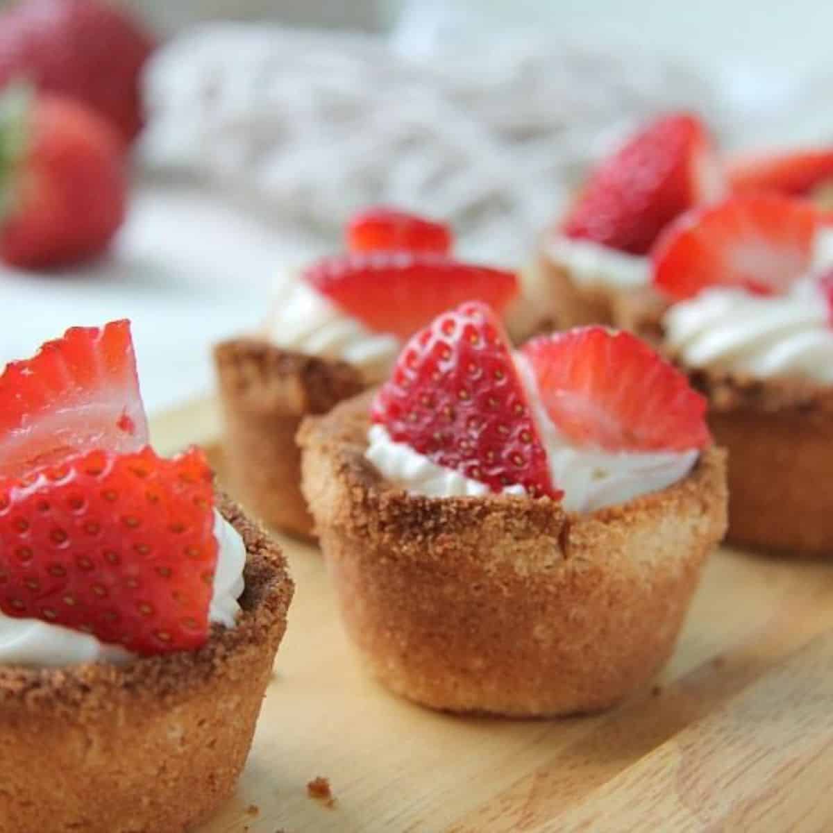 Mini cheesecakes topped with whipped cream and fresh strawberry slices, displayed on a wooden surface, inspired by keto strawberry shortcake.