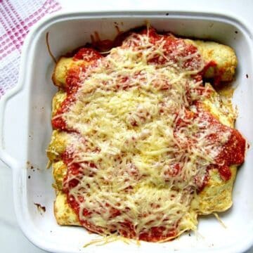 Cannelloni-shaped baked zucchini rolls topped with melted cheese and marinara sauce in a white ceramic dish.