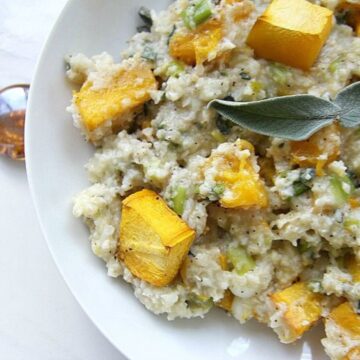 A plate of pumpkin cauliflower risotto topped with pieces of roasted butternut squash and garnished with a fresh sage leaf.