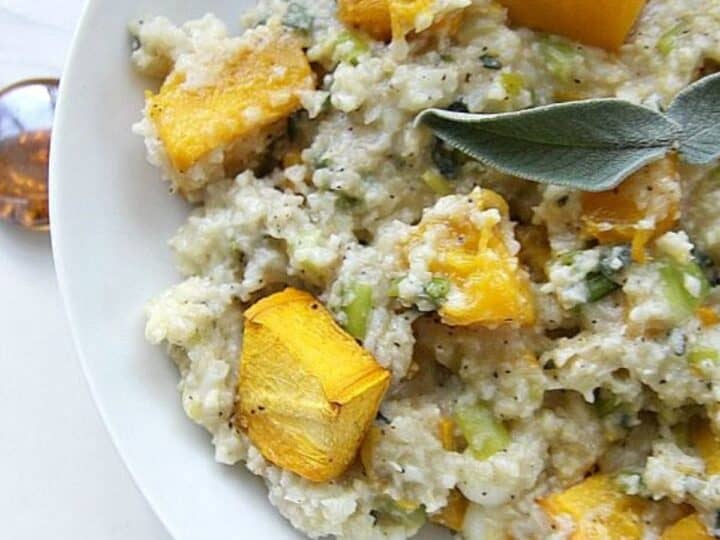 A plate of pumpkin cauliflower risotto topped with pieces of roasted butternut squash and garnished with a fresh sage leaf.