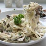A plate of creamy cabbage fettuccine pasta with mushrooms and a garnish of parsley.