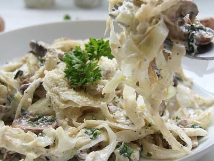 A plate of creamy cabbage fettuccine pasta with mushrooms and a garnish of parsley.