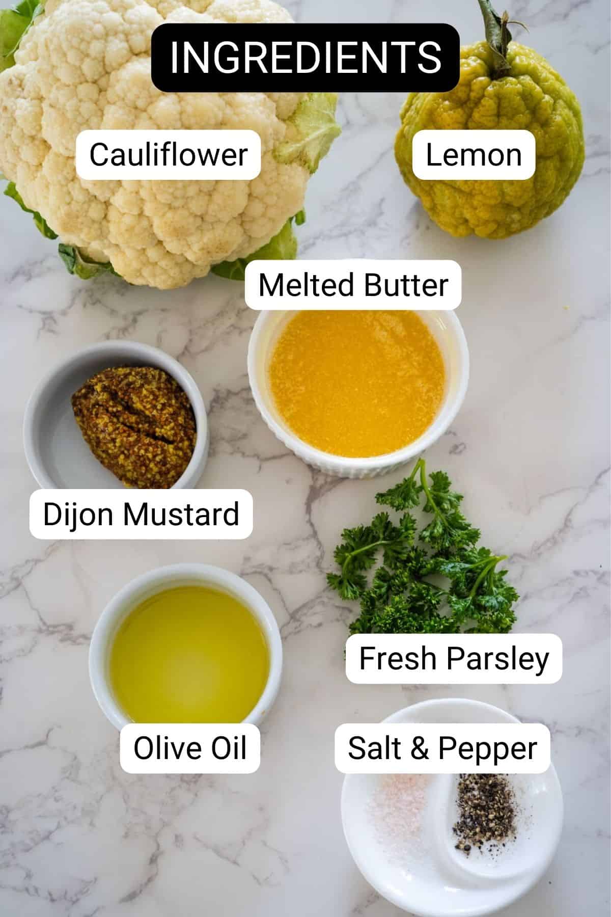 Top-down view of various ingredients labeled for a keto roasted cauliflower recipe, including cauliflower, lemon, melted butter, dijon mustard, olive oil, fresh parsley, and salt & pepper on a marble surface