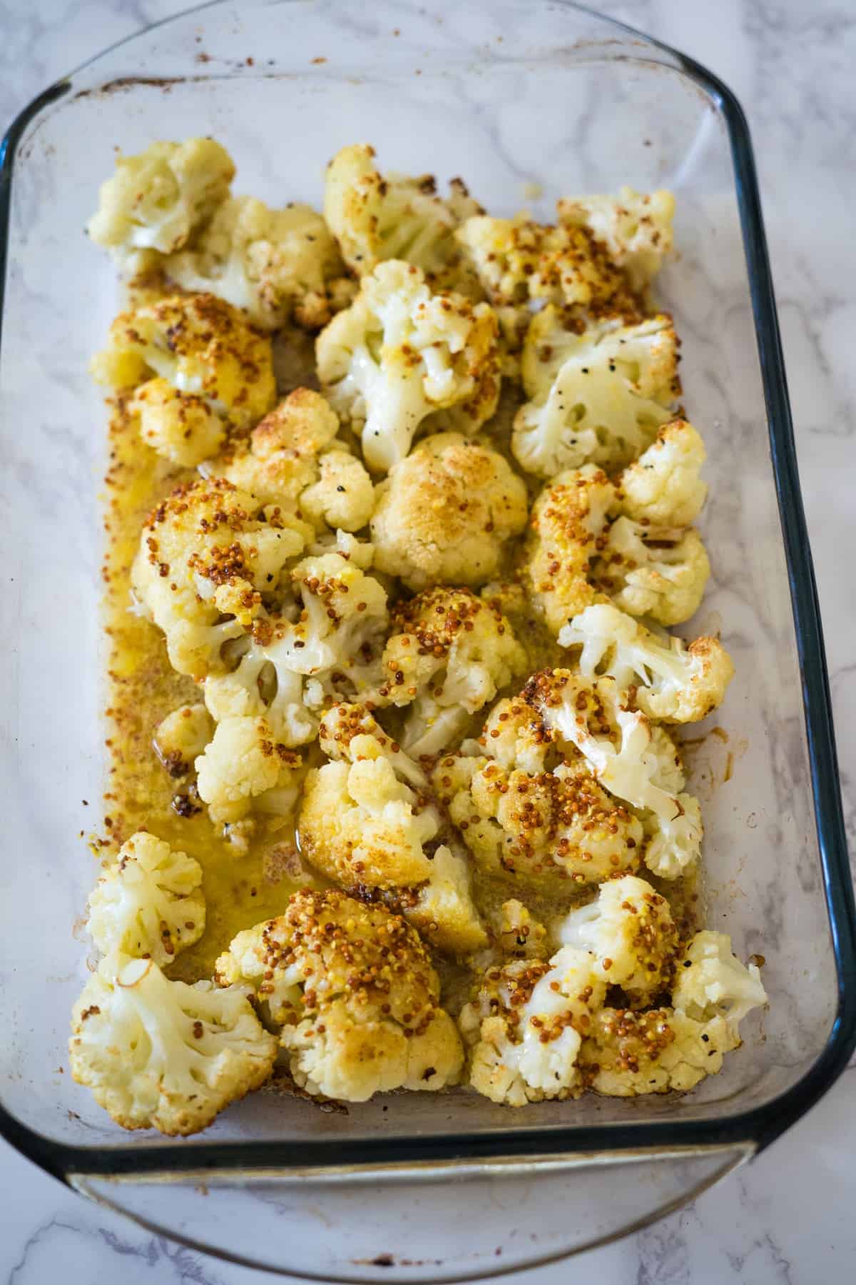 Keto roasted cauliflower with spices in a glass baking dish on a marble counter.
