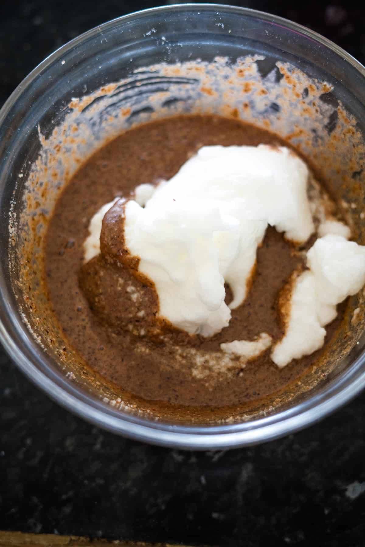 A bowl of rich chocolate hazelnut batter with a dollop of white cream on top.