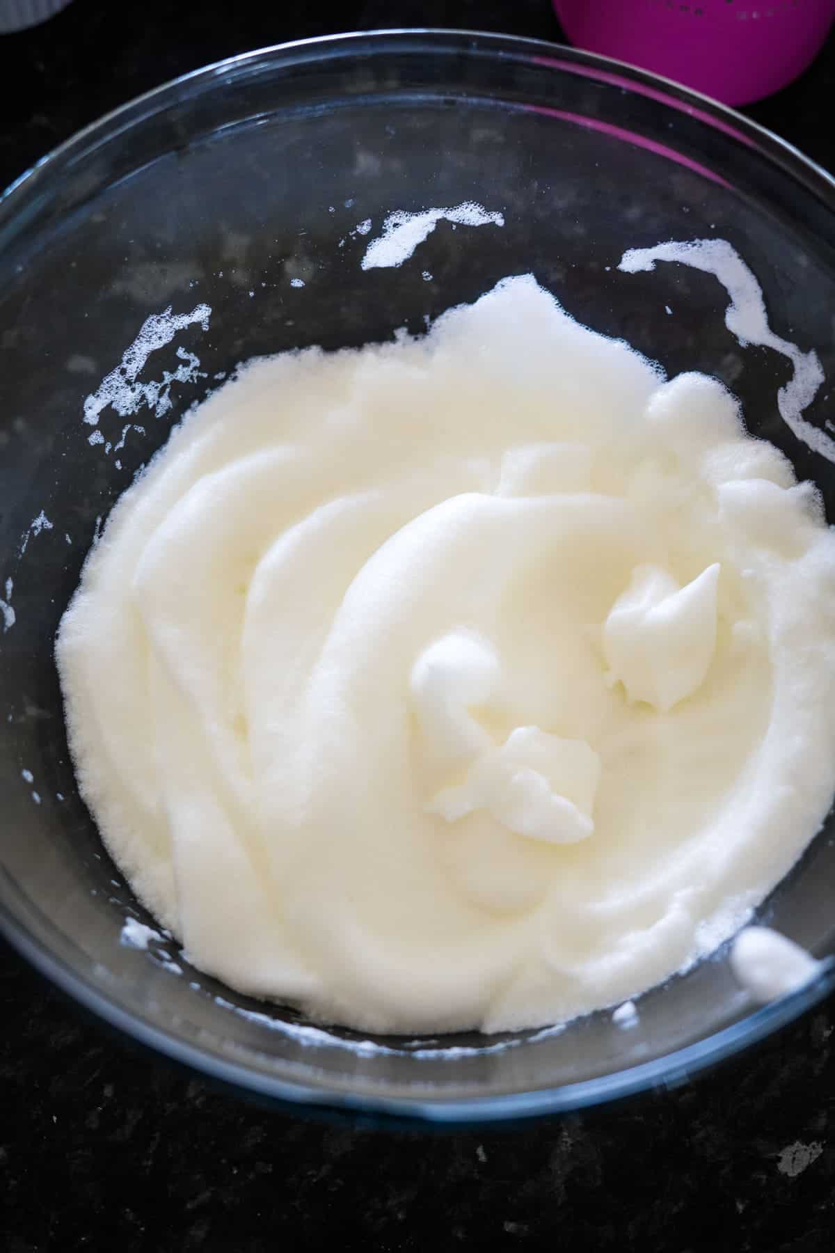 A clear glass bowl filled with whipped egg whites sits on a dark countertop, ready for a touch of chocolate hazelnut delight.