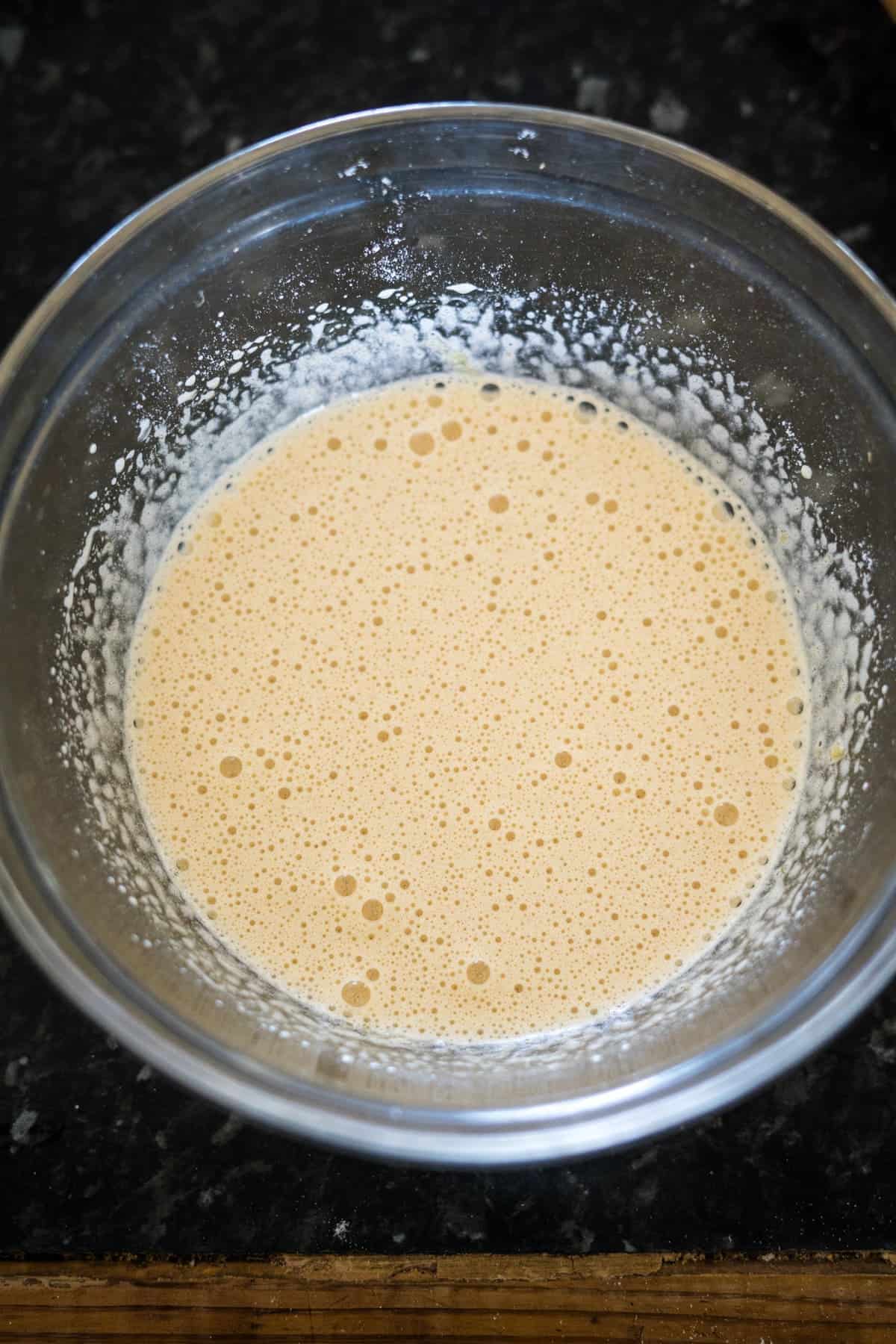 A glass bowl containing a chocolate hazelnut batter, with small bubbles visible on the surface, placed on a dark countertop.