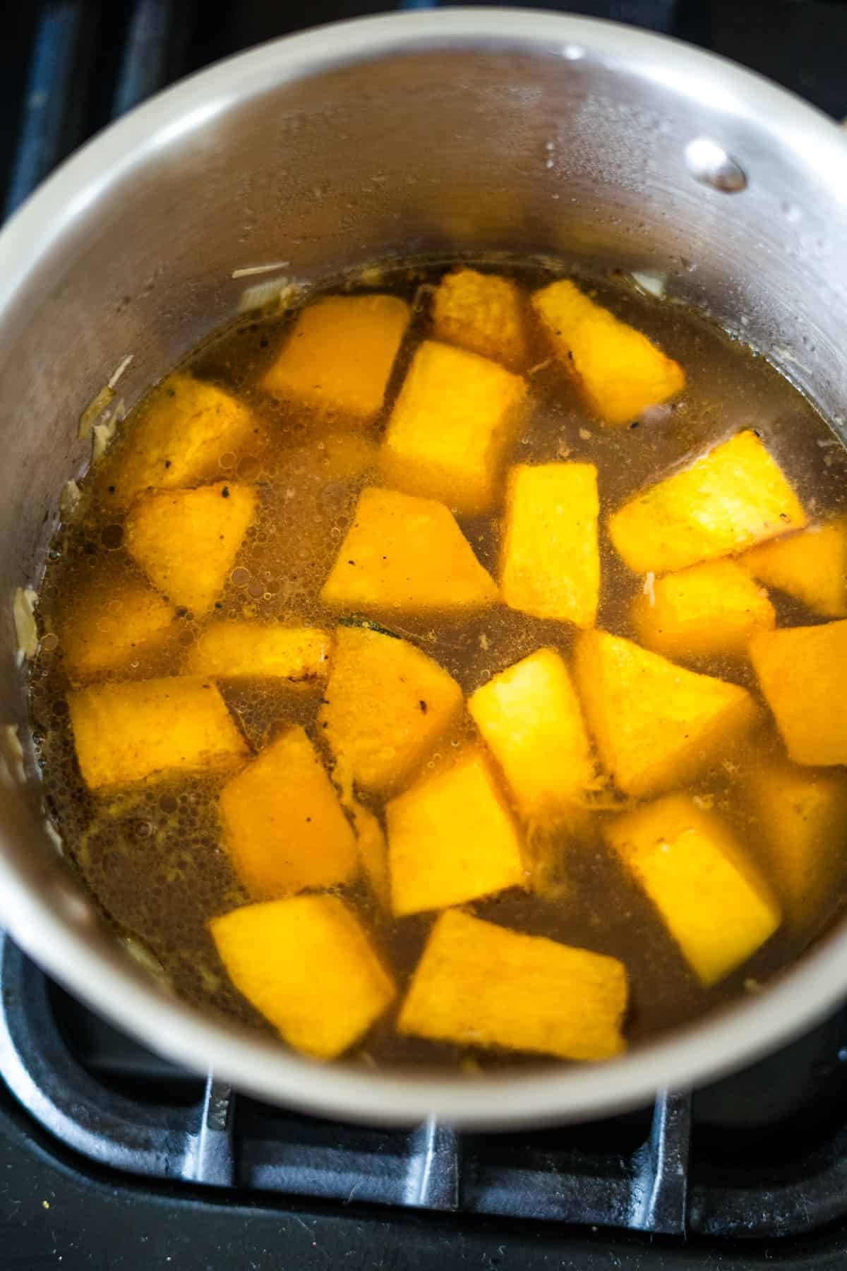 A pot contains cubed pieces of pumpkin and a hint of ginger boiling in water on a stovetop.