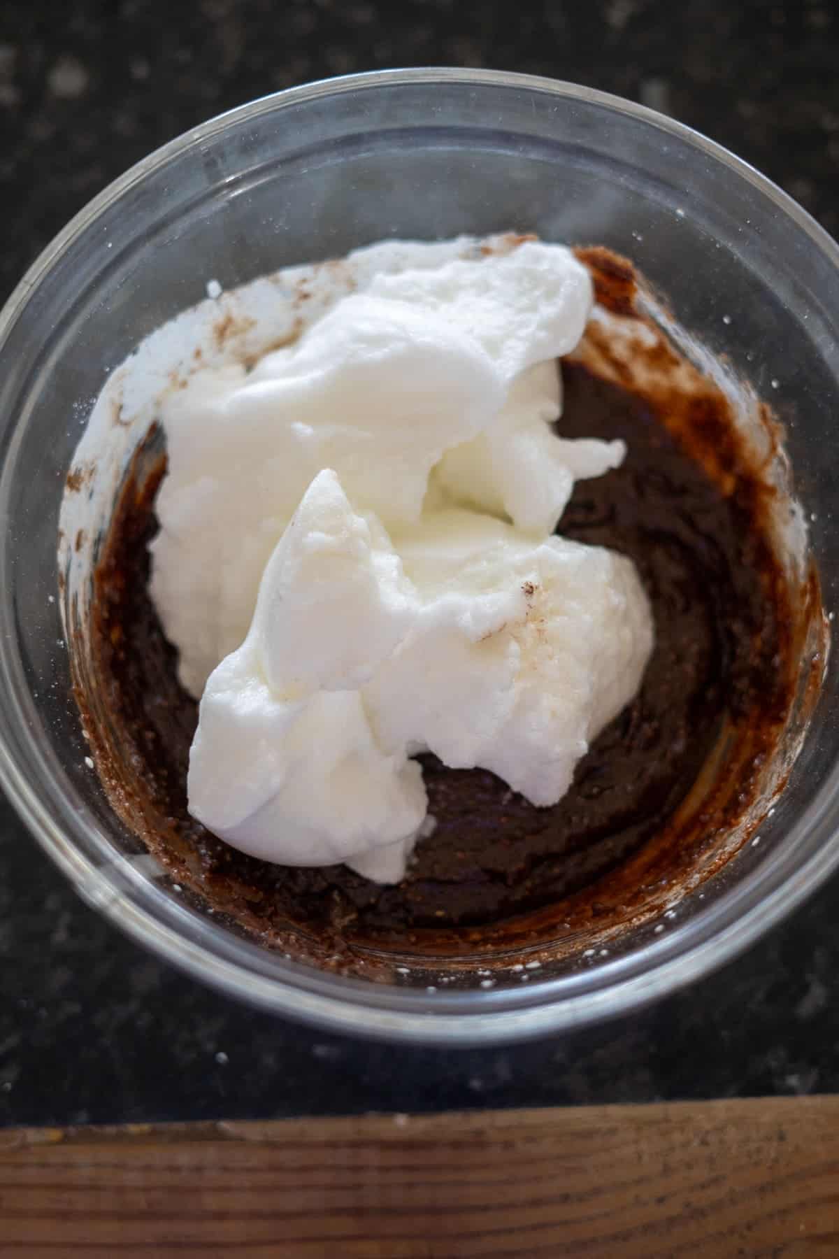 A glass bowl holds a luscious mixture of chocolate batter, whipped cream, and a hint of pecan torte essence, ready to be blended.