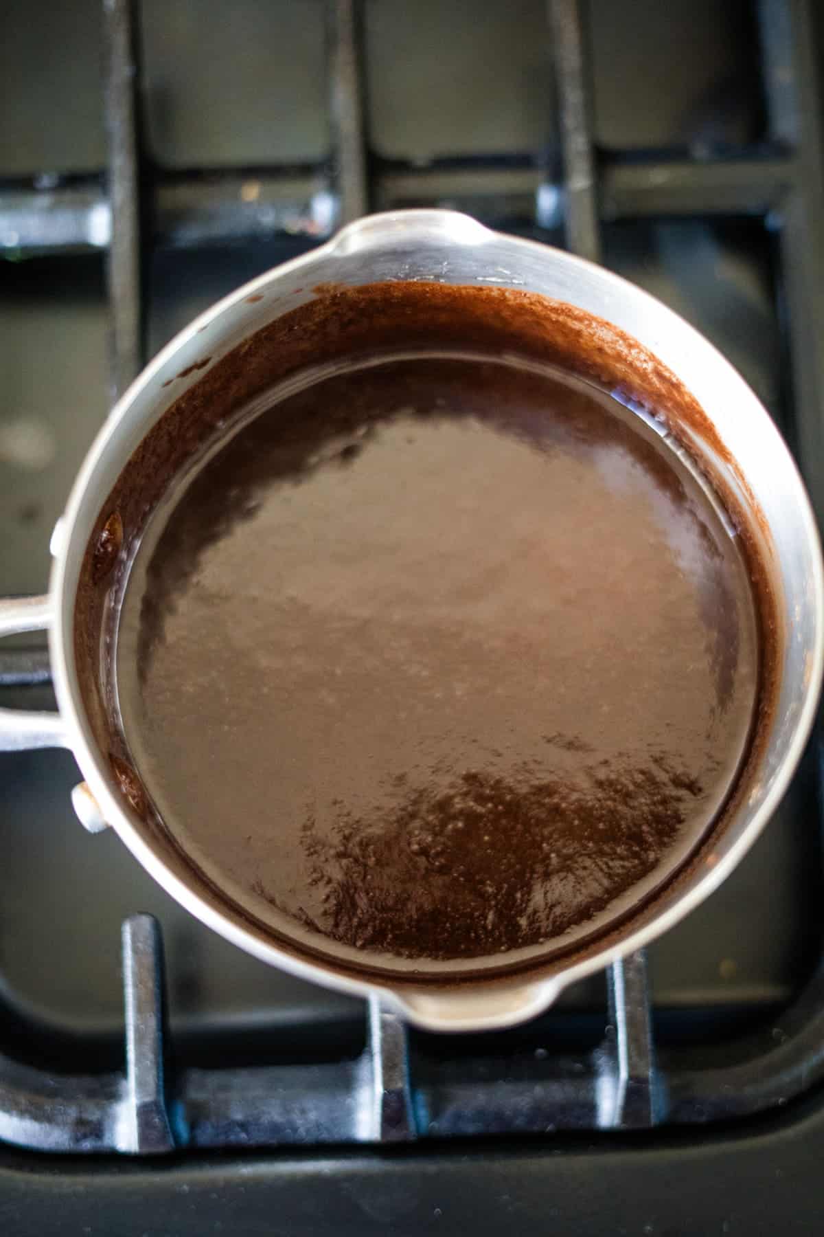 A saucepan with thick chocolate sauce simmers on the stove, reminiscent of the rich layers found in a decadent pecan torte.