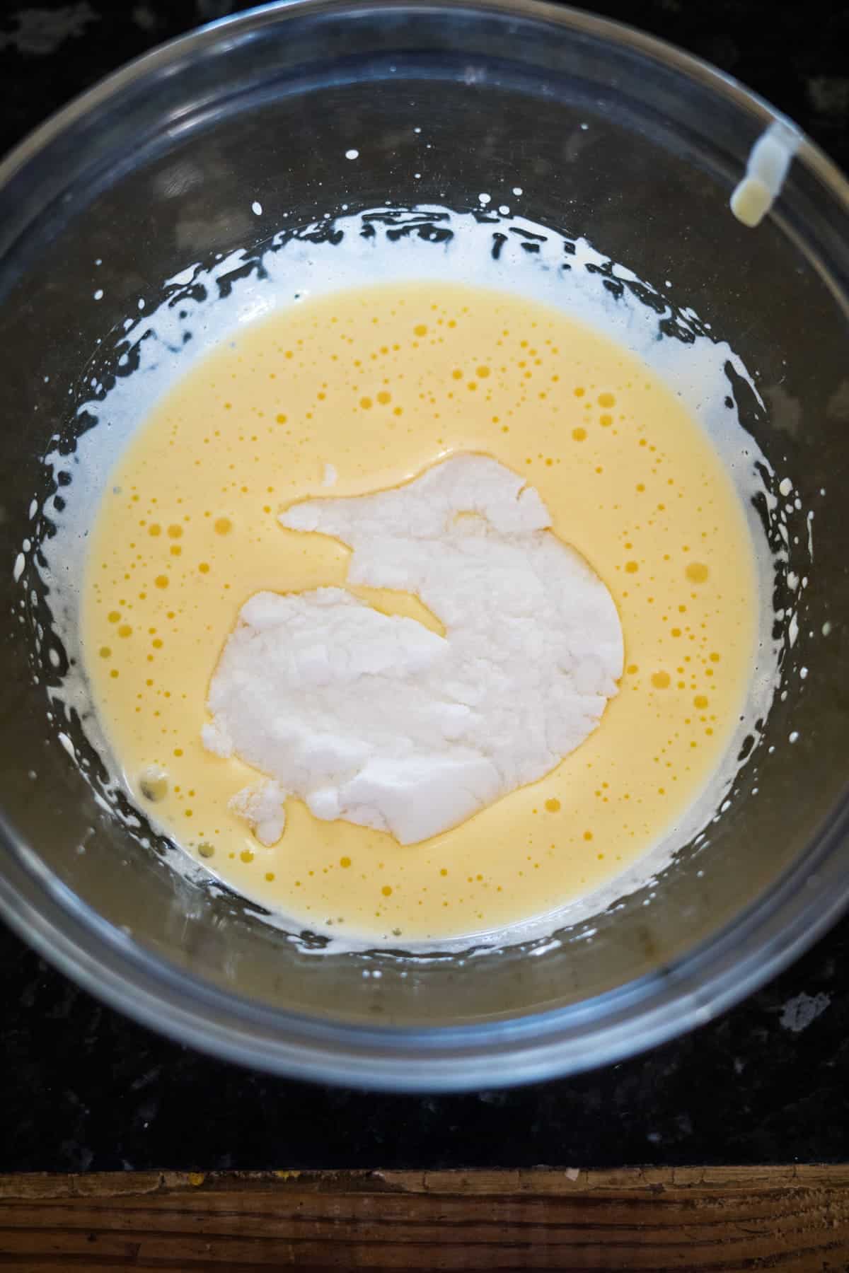 A bowl with a mixture of beaten eggs and flour, ready to create a delightful pecan torte, rests on the sleek black countertop.