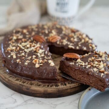 A delightful pecan torte adorned with chopped nuts, featuring a slice artfully placed on a plate.