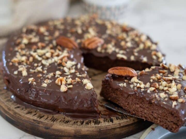 A delightful pecan torte adorned with chopped nuts, featuring a slice artfully placed on a plate.