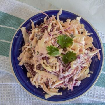 A bowl of chipotle coleslaw with shredded purple and white cabbage, garnished with parsley, on a blue plate.