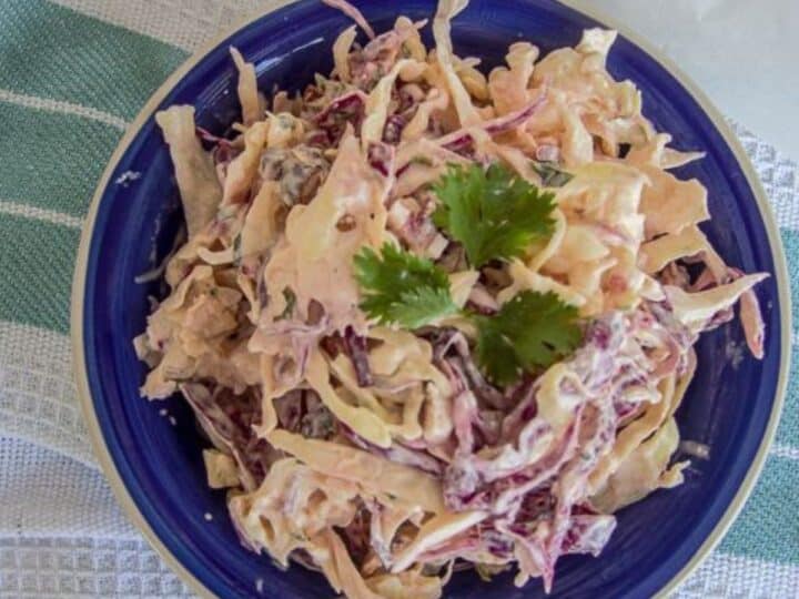A bowl of chipotle coleslaw with shredded purple and white cabbage, garnished with parsley, on a blue plate.