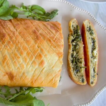 A sliced loaf of keto spinach stromboli on a white plate, filled with greens and cheese, with fresh arugula garnish.