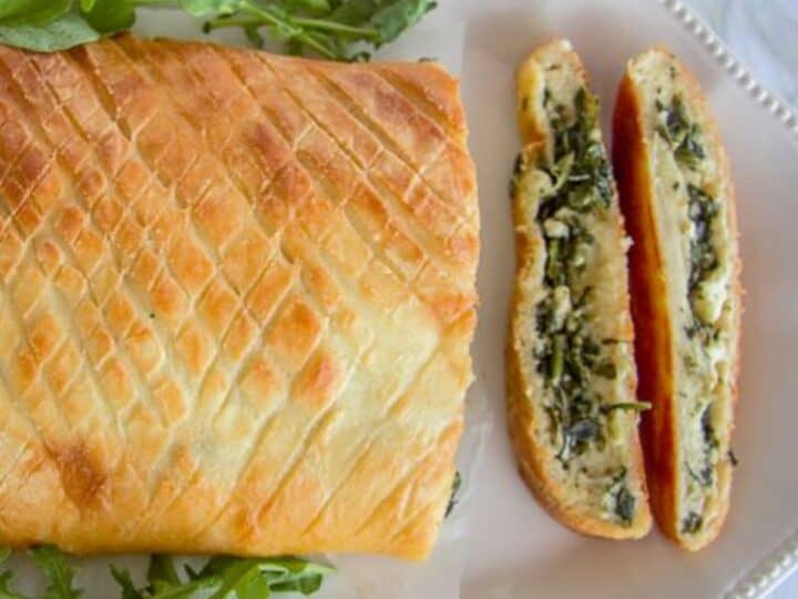 A sliced loaf of keto spinach stromboli on a white plate, filled with greens and cheese, with fresh arugula garnish.