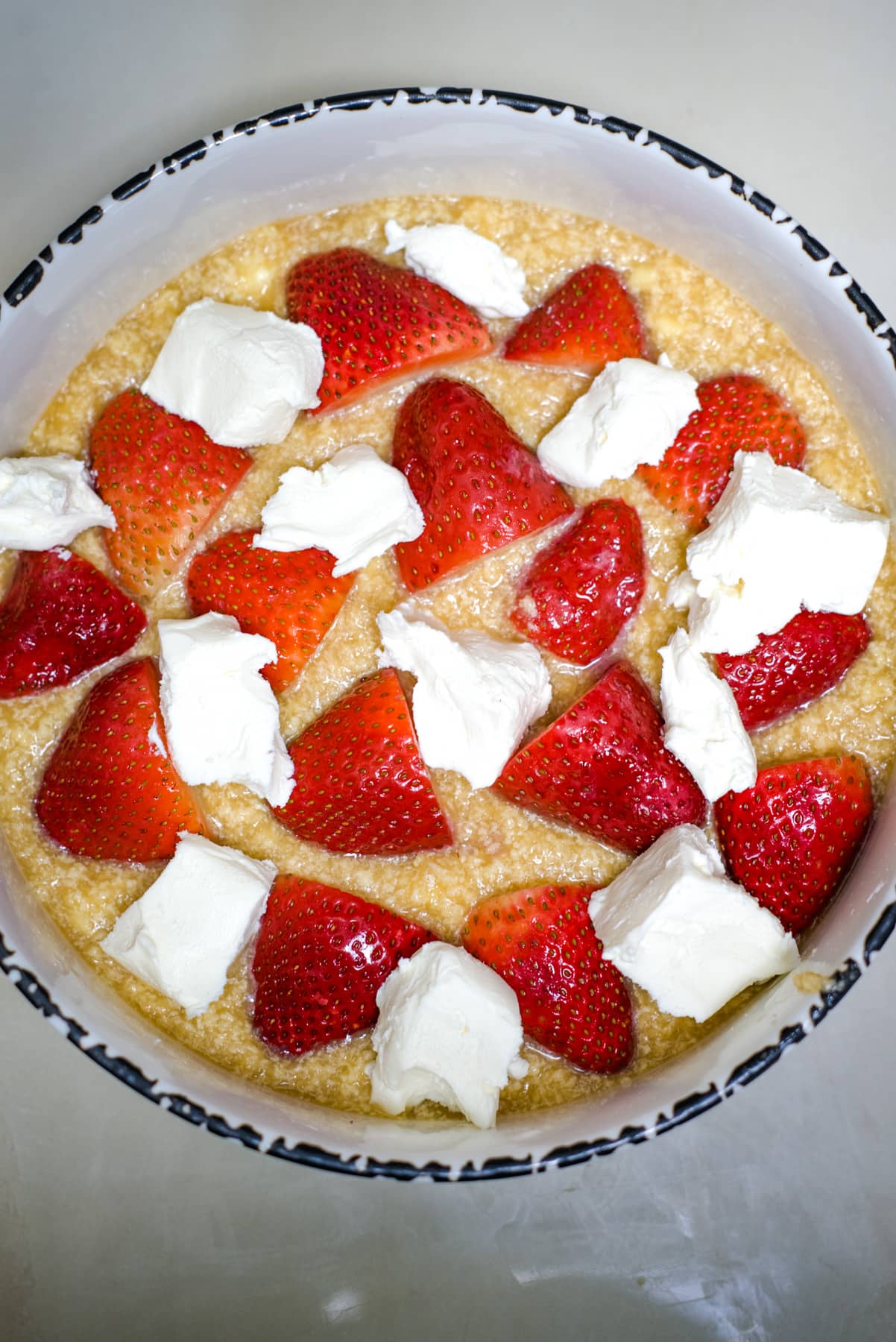 circular baking dish with strawberries and cream cheese chunks on a cobbler batter