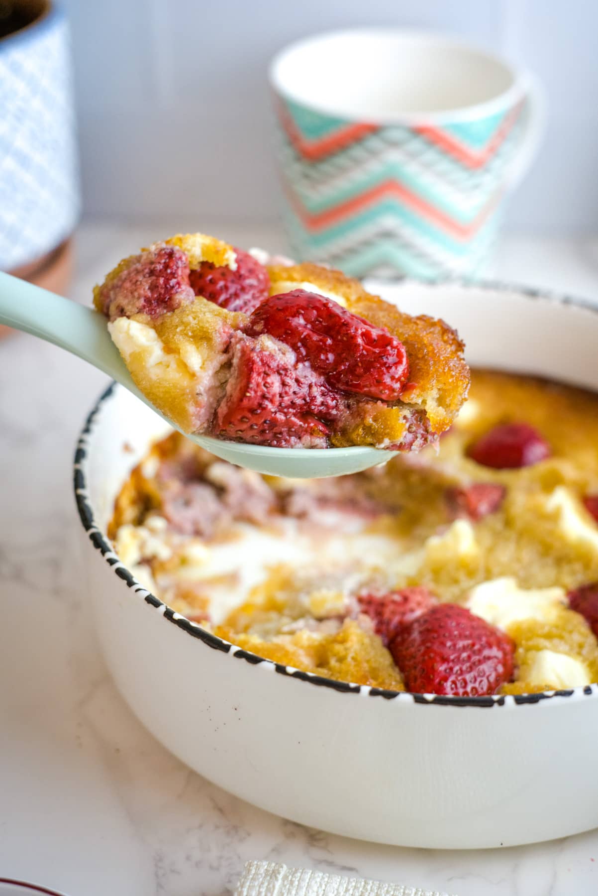 A serving spoon loaded with a serving of strawberry cream cheese cobbler