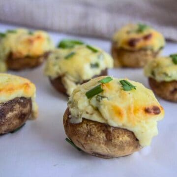 Jalapeno popper stuffed mushrooms topped with melted cheese and chives rest invitingly on a white surface.