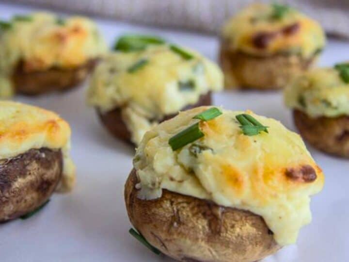 Jalapeno popper stuffed mushrooms topped with melted cheese and chives rest invitingly on a white surface.